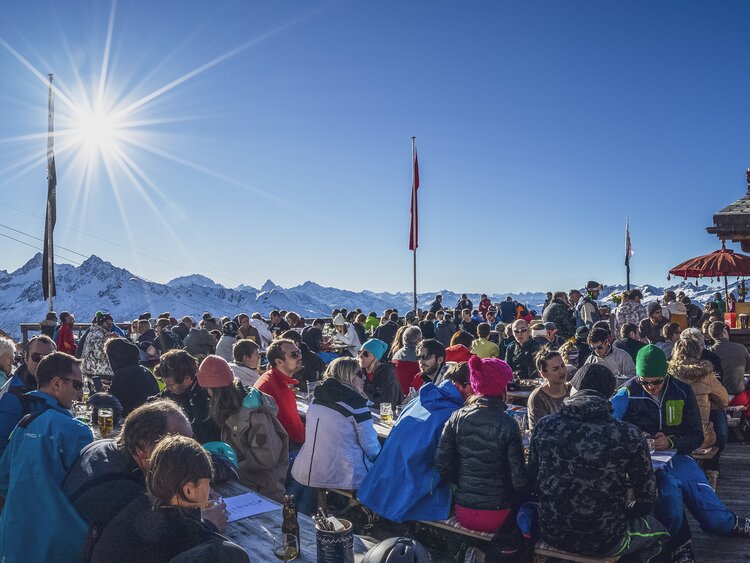 Skifahrer wie auch Fussgänger geniessen ihr Mittagessen auf der Terrasse des Chalet Güggel bei Sonnenschein. | © Davos Klosters Mountains