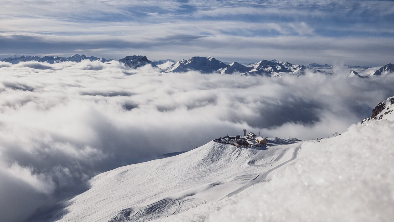 Aufnahme aus der Ferne mit Sicht auf die Jatzhütte Davos welche über den Wolken ersichtlich ist. | © Davos Klosters Mountain
