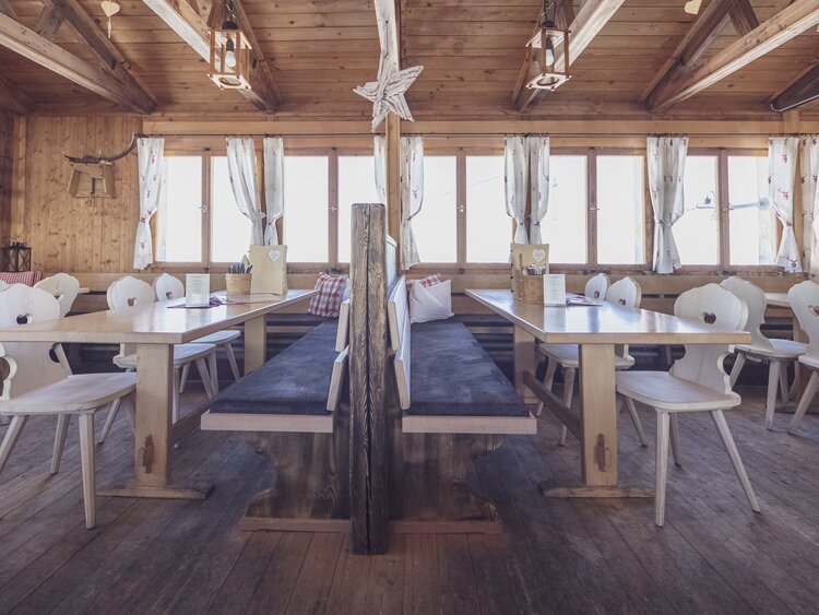 Lange schlichte Holztische mit Sitzbänken und Stühlen stehen bereit für die Gäste der Hubelhütte. | © Davos Klosters Mountains