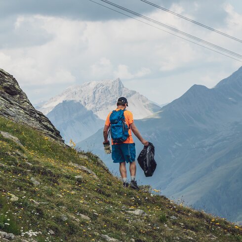 Ein Helfer sammelt Abfall auf dem Berg ein, er ist mit Handschuhen und Müllsack ausgerüstet. | © Davos Klosters Mountains