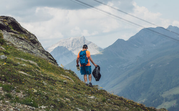 Ein Helfer sammelt Abfall auf dem Berg ein, er ist mit Handschuhen und Müllsack ausgerüstet. | © Davos Klosters Mountains
