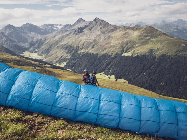 Der Pilot ist gegen den Gleitschirm gerichtet und ist bereit für den Abflug mit dem Gast. | © Davos Klosters Mountains