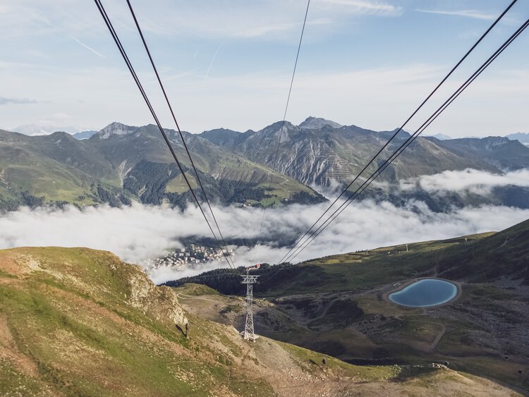 Der Blick geht den Seilen der Gondel Jakobshorn entlang ins Tal, wo ein Wolkenmeer liegt. | © Davos Klosters Mountains