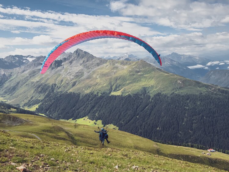Der Gleitschirm hebt ab und die beiden Passagiere fliegen bei einem Tandemflug hinunter nach Davos.  | © Davos Klosters Mountains