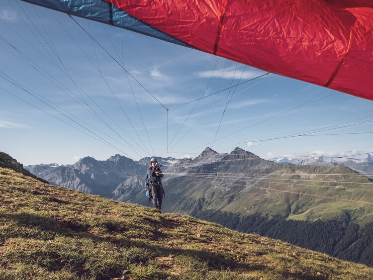 Der Pilot hält den rot-blauen Gleitschirm mit den Steuerleinen fest, dieser erhebt sich in die Luft. | © Davos Klosters Mountains
