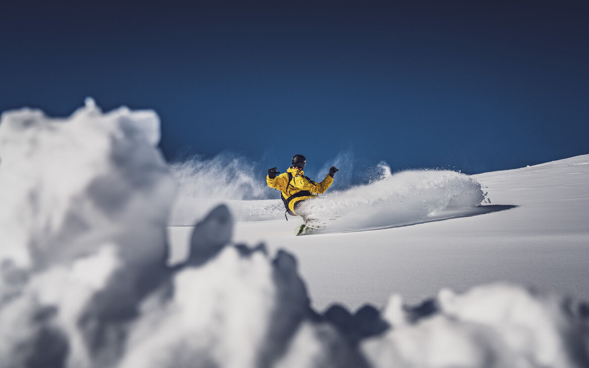 Snowboarder mit gelber Jacke beim Freeriden im Pulverschnee in den Davos Klosters Mountains. | © Davos Klosters Mountains