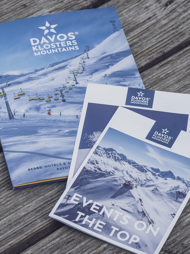 Präsentationsmappe und Broschüren | © Davos Klosters Mountains Präsentationsmappe und Broschüren liegen auf dunklem Holztisch. | © Davos Klosters Mountains