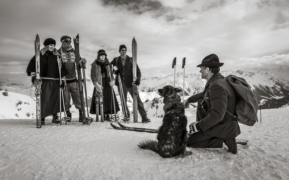 Eine Gruppe Skifahrer nostalgisch gekleidet hört dem Rettungschef mit Hund zu.  | © Davos Klosters Mountains