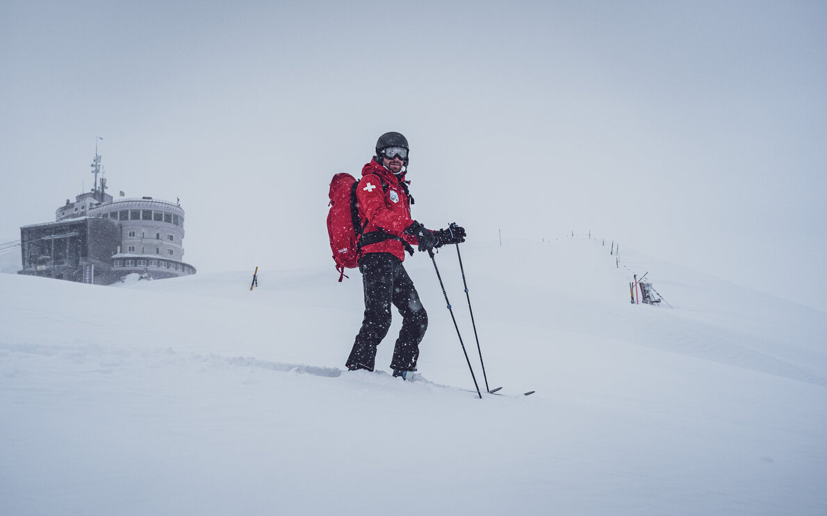 Michi vom Rettungsdienst Jakobshorn ist mit den Skiern im Einsatz, hinter ihm die Bergstation Jakobshorn.  | © Davos Klosters Mountains
