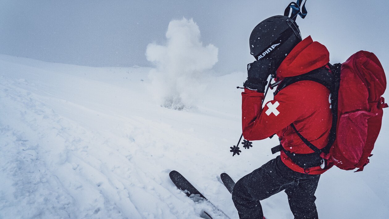 Der Patrouilleur vom Jakobshorn hält sich die Ohren zu und der Sprengkörper explodiert im Schnee. | © Davos Klosters Mountains