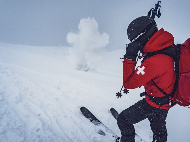 Der Patrouilleur vom Jakobshorn hält sich die Ohren zu und der Sprengkörper explodiert im Schnee. | © Davos Klosters Mountains