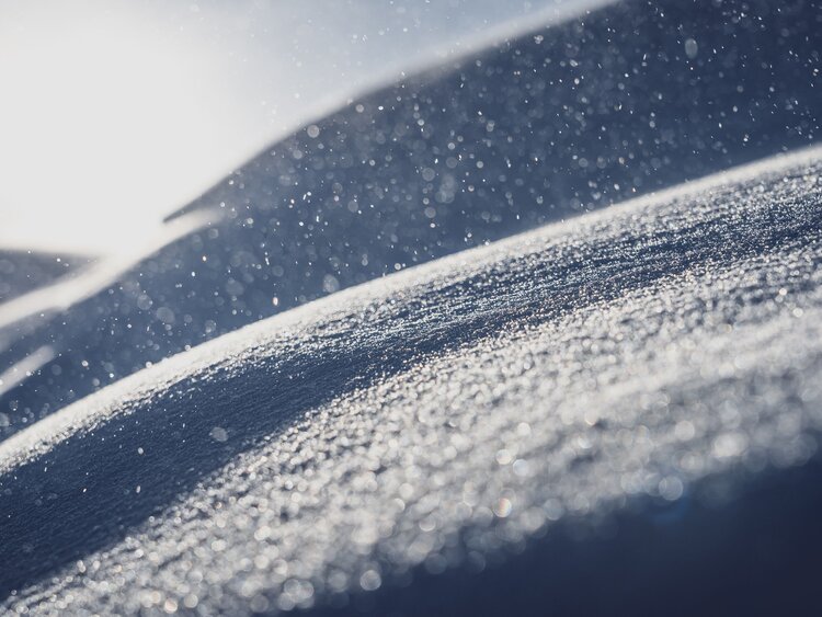 Glitzernde Schneeflocken fliegen in der Luft und werden von der Sonne beleuchtet.  | © Davos Klosters Mountains