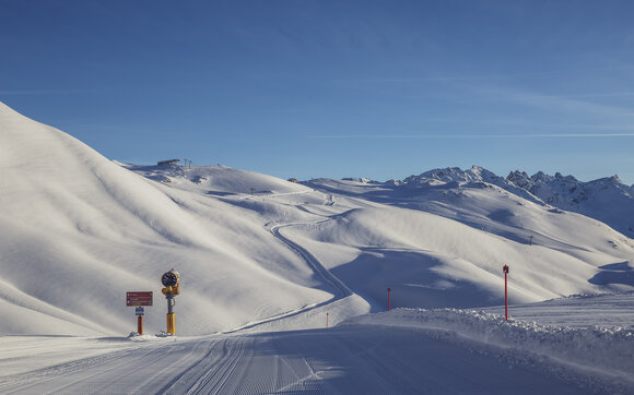 Fokus auf frisch präparierte Piste mit verschneitem Skigebiet im Hintergrund. | © Davos Klosters Mountains