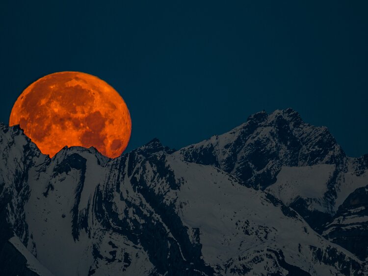 Ein roter Vollmond erhebt sich hinter dem verschneiten Bergkamm. | © Davos Klosters Mountains