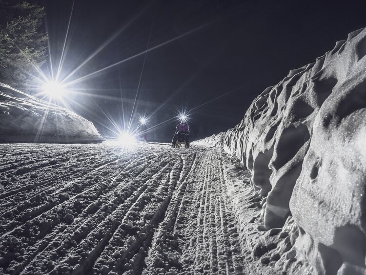 Mädchen mit Taschenlampe schlittelt auf der Nachtpiste hinunter. | © Davos Klosters Mountains