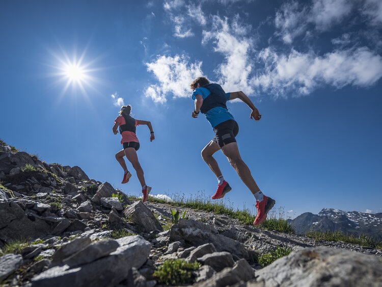 Zwei Trailrunner rennen im Gleichschritt und mit viel Körperspannung dem Berg hinauf in Richtung der scheinenden Sonne.  | © Davos Klosters Mountains