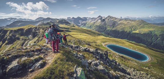 Eine Gruppe von Wanderer blickt vom Grat hinab auf den tiefblauen Stadlersee.