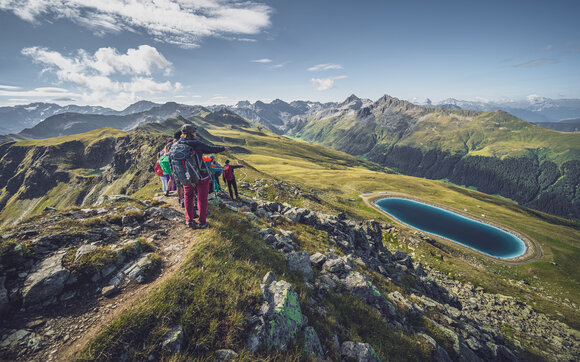 Eine Gruppe von Wanderer blickt vom Grat hinab auf den tiefblauen Stadlersee. | © Davos Klosters Mountains