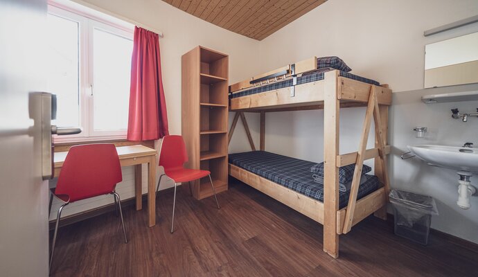 Zimmer mit Stockbett, Kleiderablage, Lavabo und Schreibtisch mit Stuhl | © Davos Klosters Mountains 