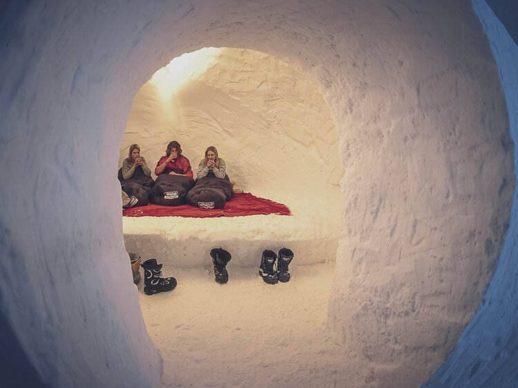 Schnee Iglu mit 3 im Schlafsack sitzenden, Tee trinkenden Personen | © Davos Klosters Mountains