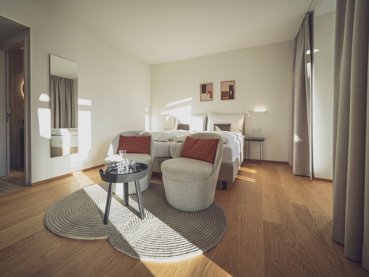 Helles Doppelzimmer mit Holzboden, Salontisch und Sitzgelegenheiten | © Davos Klosters Mountains 