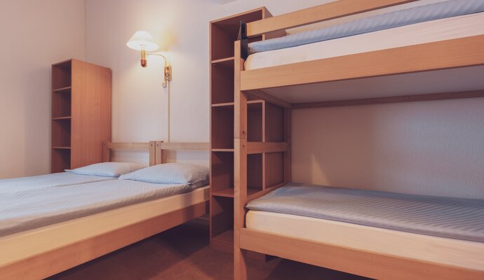 Mehrbettzimmer mit einem Doppelbett und einem Stockbett mit Bettwäsche und Ablageschränken | © Davos Klosters Mountains