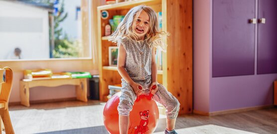 Ein Mädchen sitzt auf einem roten Ball und hüpft durch den Globi Kids Club im Hotel Waldhuus Davos.