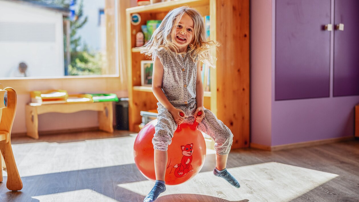 Ein Mädchen sitzt auf einem roten Ball und hüpft durch den Globi Kids Club im Hotel Waldhuus Davos. | © DDO - davos.ch | Martin Bissig