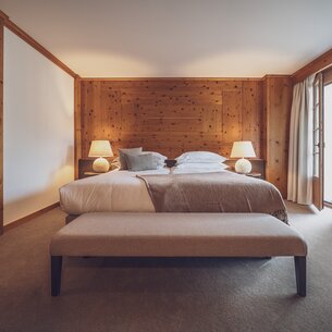 Double bed room with bed linen, bedside lamp and clothes bench  | © Davos Klosters Mountains 